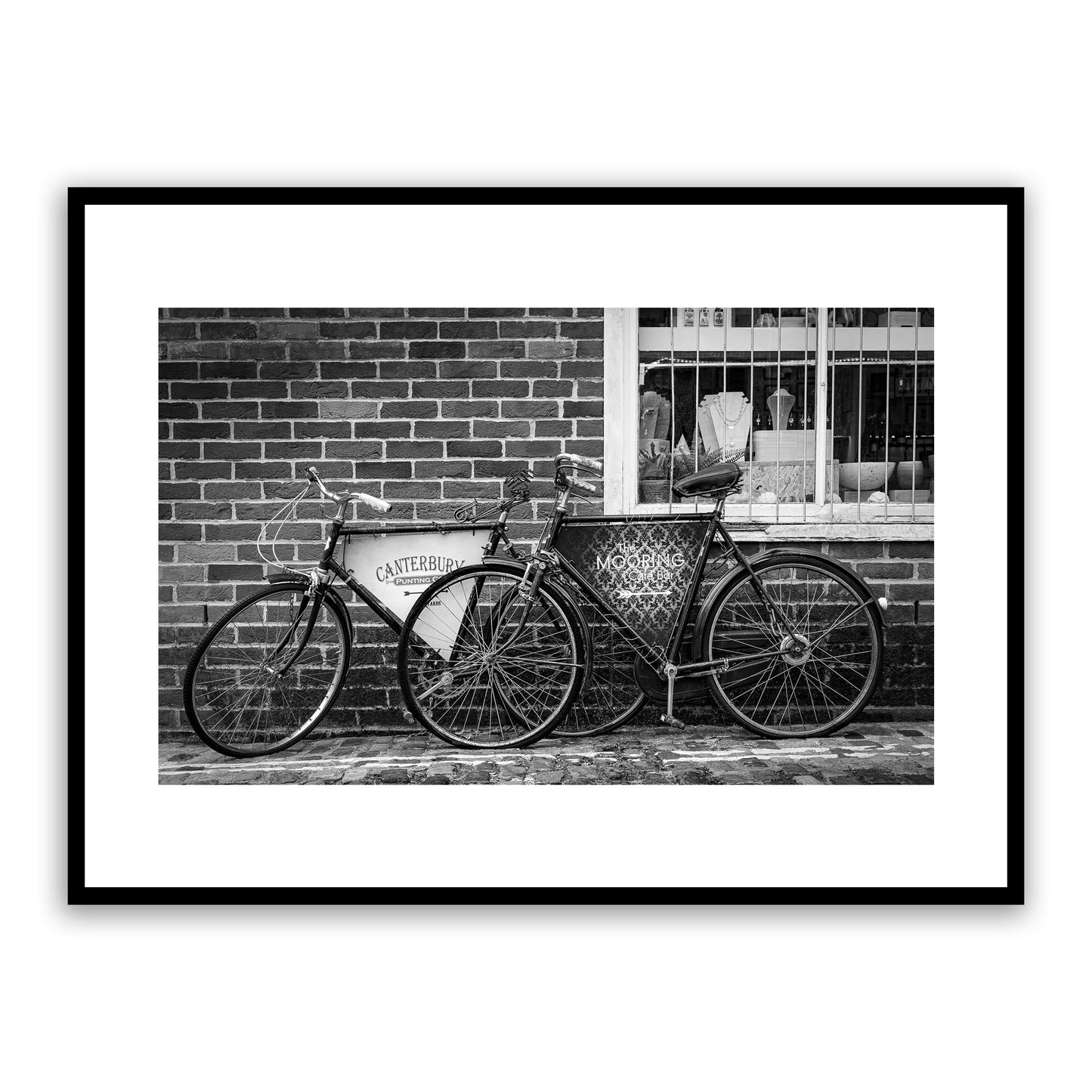 Old vintage bikes on the charming, cobbled, Water Lane, Canterbury, Kent, England, with signs for Canterbury Punting Company and The Mooring Café Bar. Rock, Paper, Scissors store visible through window. Fine art black and white photography print for sale.